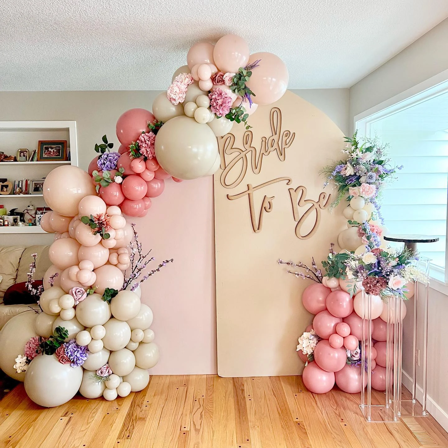 A spring-themed bridal shower photo backdrop with a pink and cream balloon arch and flowers.