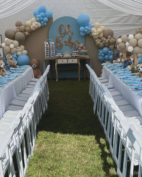 A 'we can barely wait' teddy bear themed baby shower with long tables and a balloon arch in dusty blue, tan, and cream.
