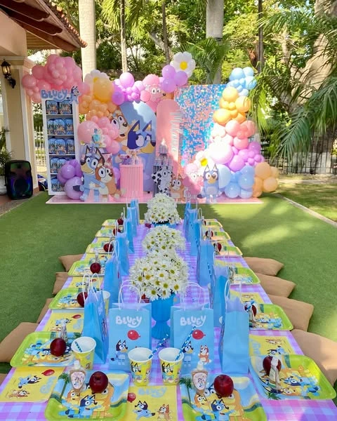 Outdoor Bluey birthday party with a long, low picnic table and a large pastel balloon backdrop.