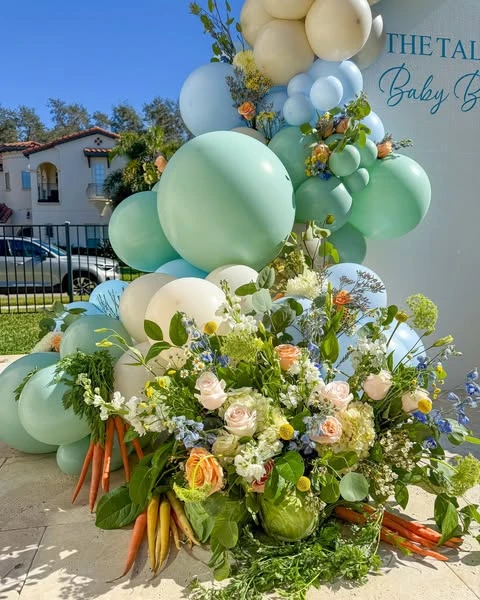 A of a floral arrangement for a Peter Rabbit baby shower, featuring fresh carrots and leafy greens mixed with pink roses and wildflowers.