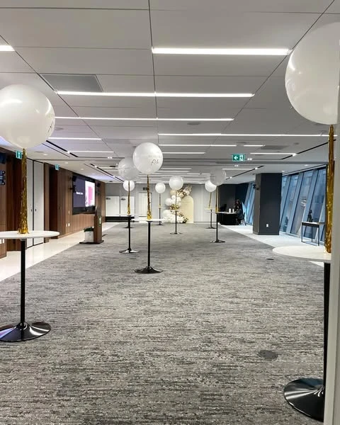 A spacious retirement party venue decorated with large white and gold balloons on cocktail tables.