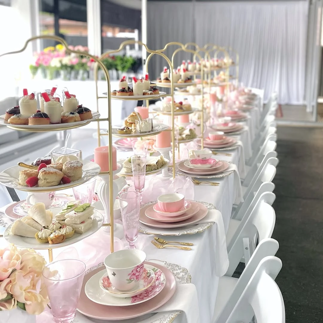 An elegant tea party bridal shower table set with individual gold tiered stands filled with pastries and sandwiches at each place setting.