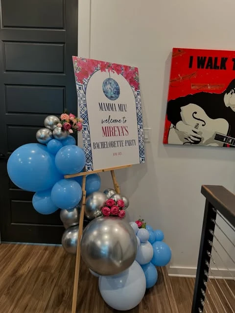 A Mamma Mia bachelorette party welcome sign on an easel, decorated with blue and silver balloons.