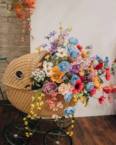 A vintage wicker pram overflowing with a colorful wildflower bouquet for a baby shower.