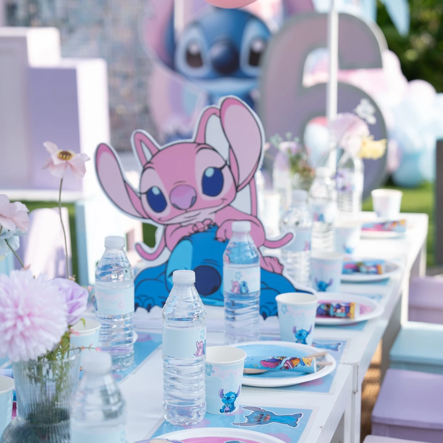 A kids' party table with an Angel character centerpiece and Stitch-themed paper plates and cups.