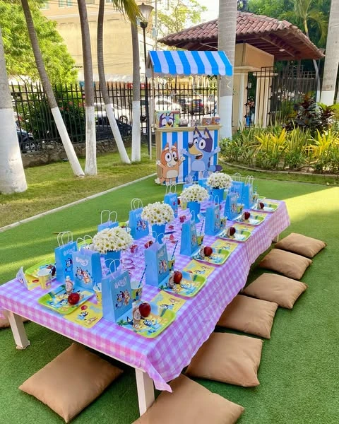 Low picnic table with floor cushions for a Bluey party, with a character-themed cart in the background.