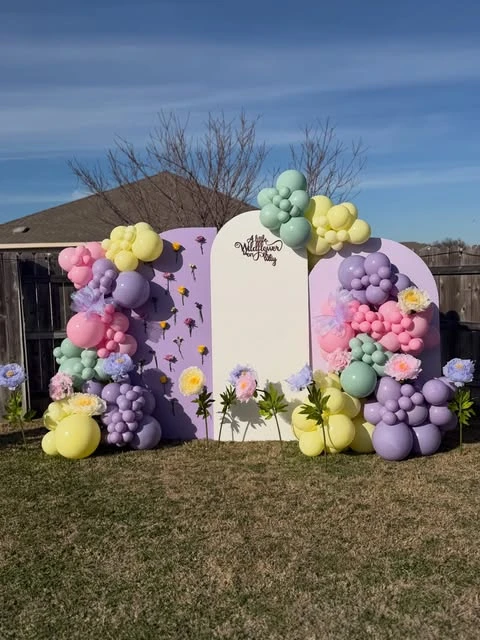 Pastel wildflower baby shower backdrop with balloons and signage.