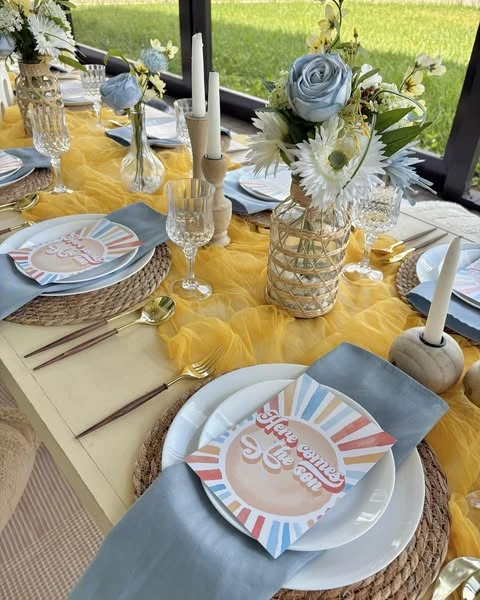 of a baby shower place setting with a rattan charger, blue napkin, and retro sun-themed card.