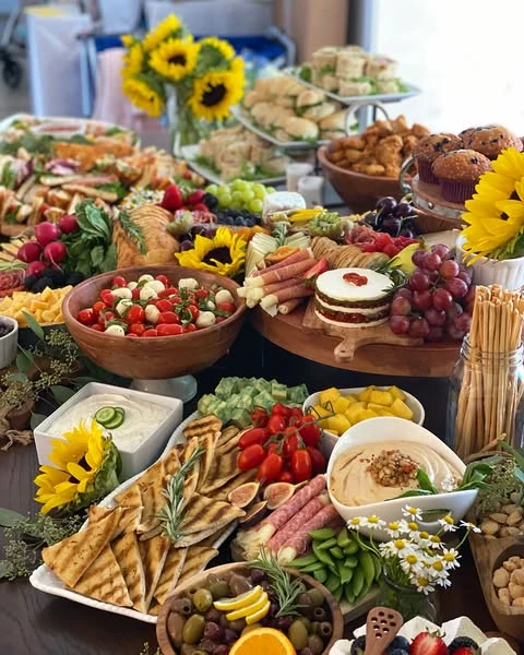A section of a baby shower grazing table with bowls of dips, caprese salad, grilled pita bread, and small sunflower decorations.