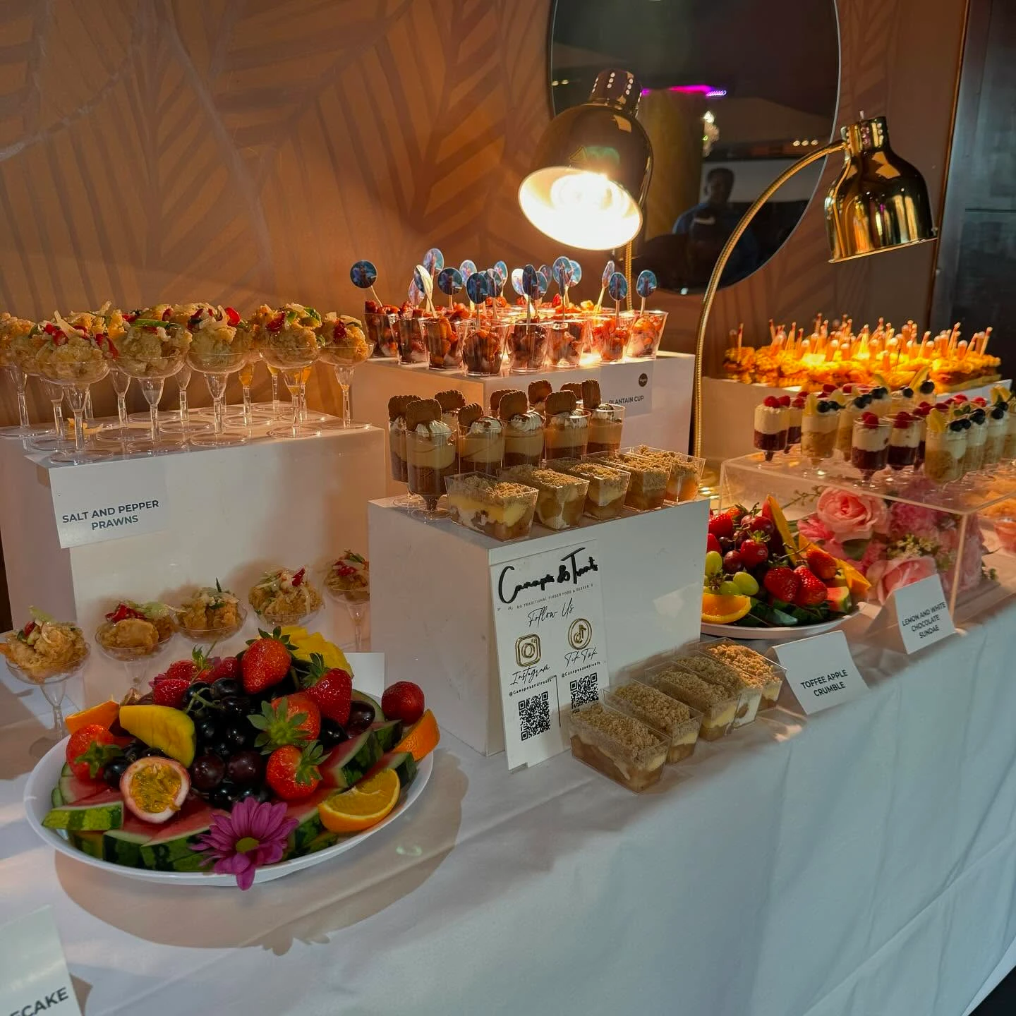 A dessert and appetizer station at a baby shower, using clear acrylic stands to display individual portions of prawns and desserts.