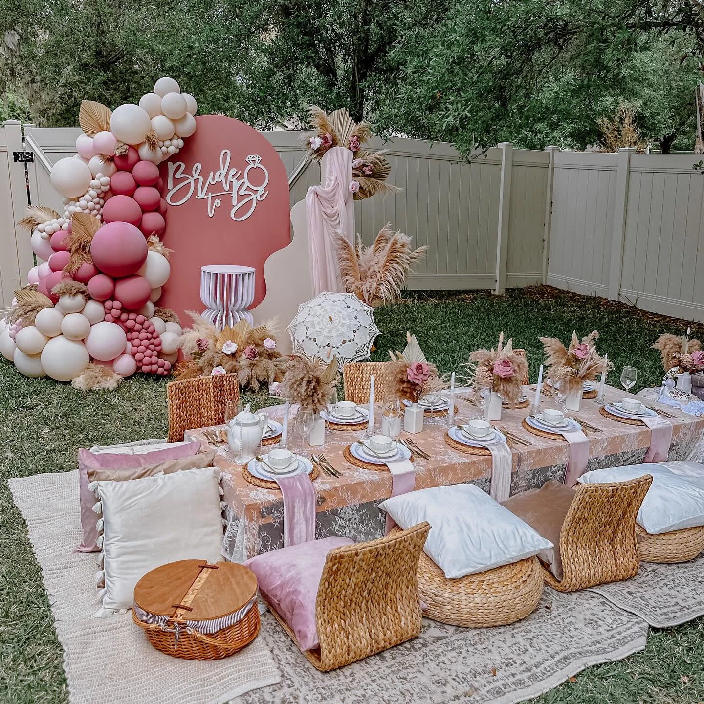 A boho-themed bridal shower tea party picnic in a backyard with a dusty rose balloon arch.