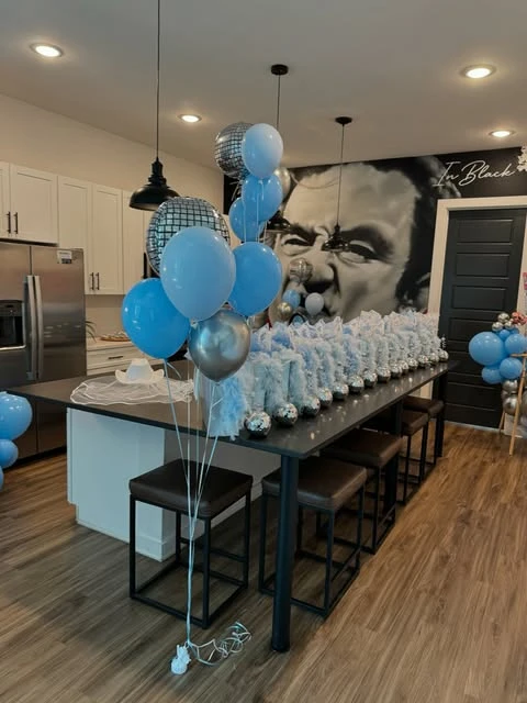 A party favor station for a Mamma Mia bachelorette with gift bags and balloon bouquets on a long table.