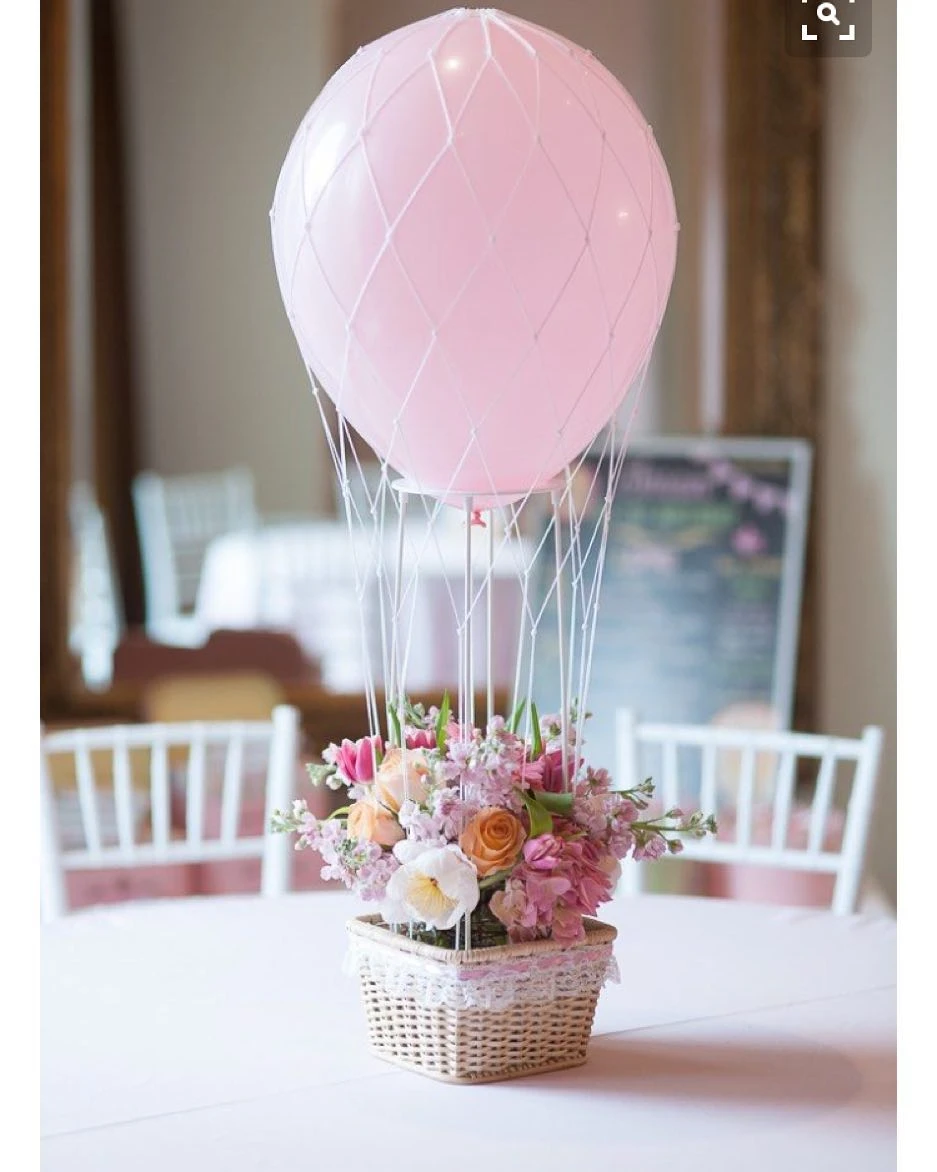 A hot air balloon themed baby shower centerpiece with a wicker basket of flowers and a large pink balloon.