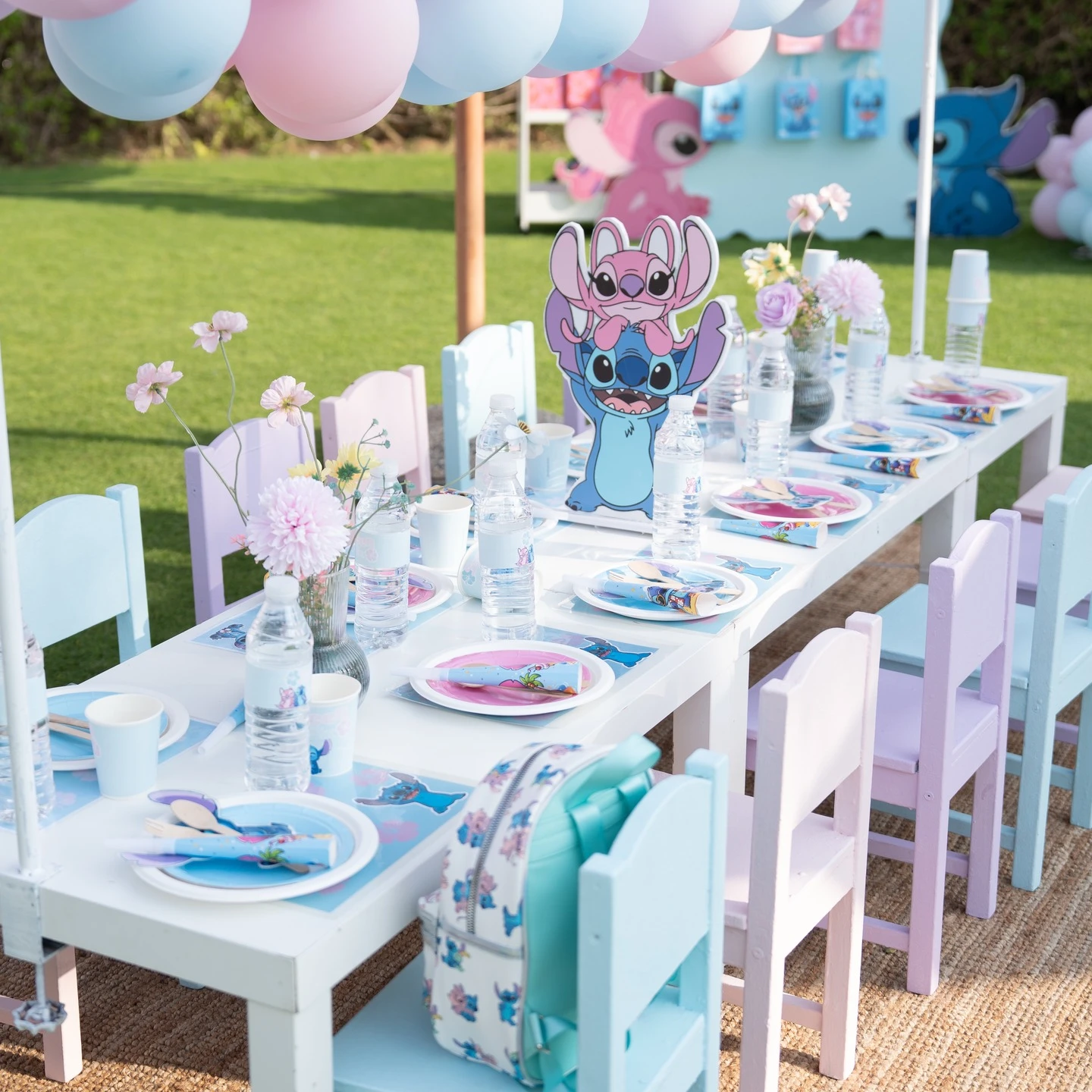A child's party table with a Stitch and Angel centerpiece, themed placemats, and alternating pastel blue and purple chairs.