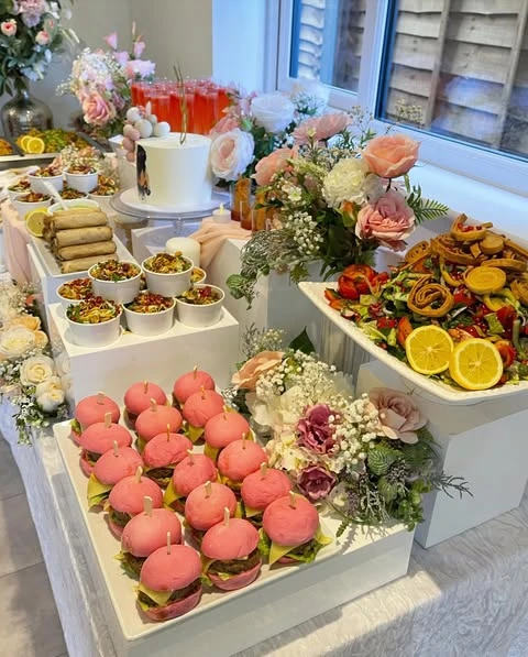 A spring bridal shower food table featuring trays of pink sliders and fresh salads.
