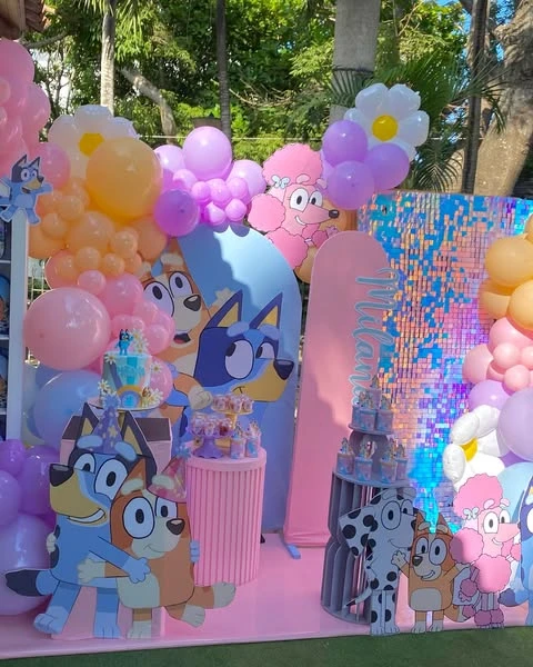 Pastel balloon arch and large Bluey character cutouts used as a party backdrop.
