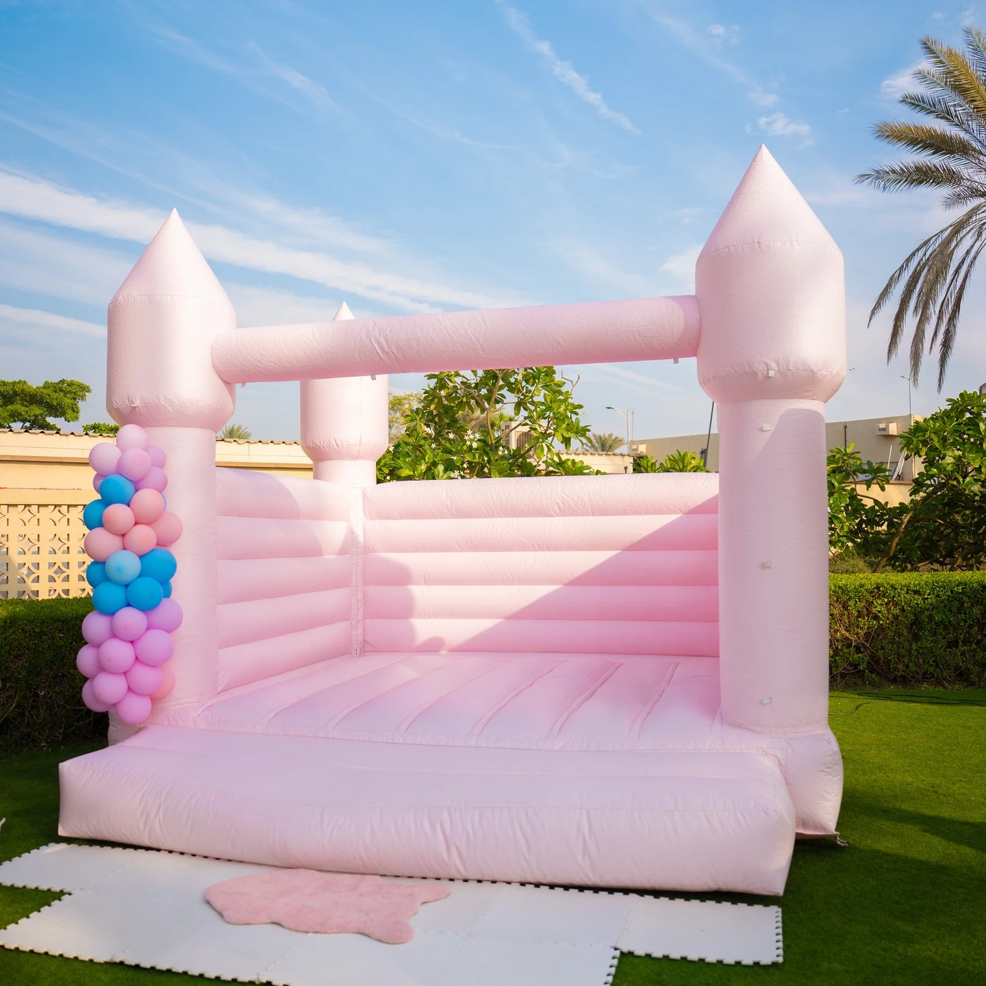 A large, pastel pink inflatable bounce house castle set up on a green lawn for a party.