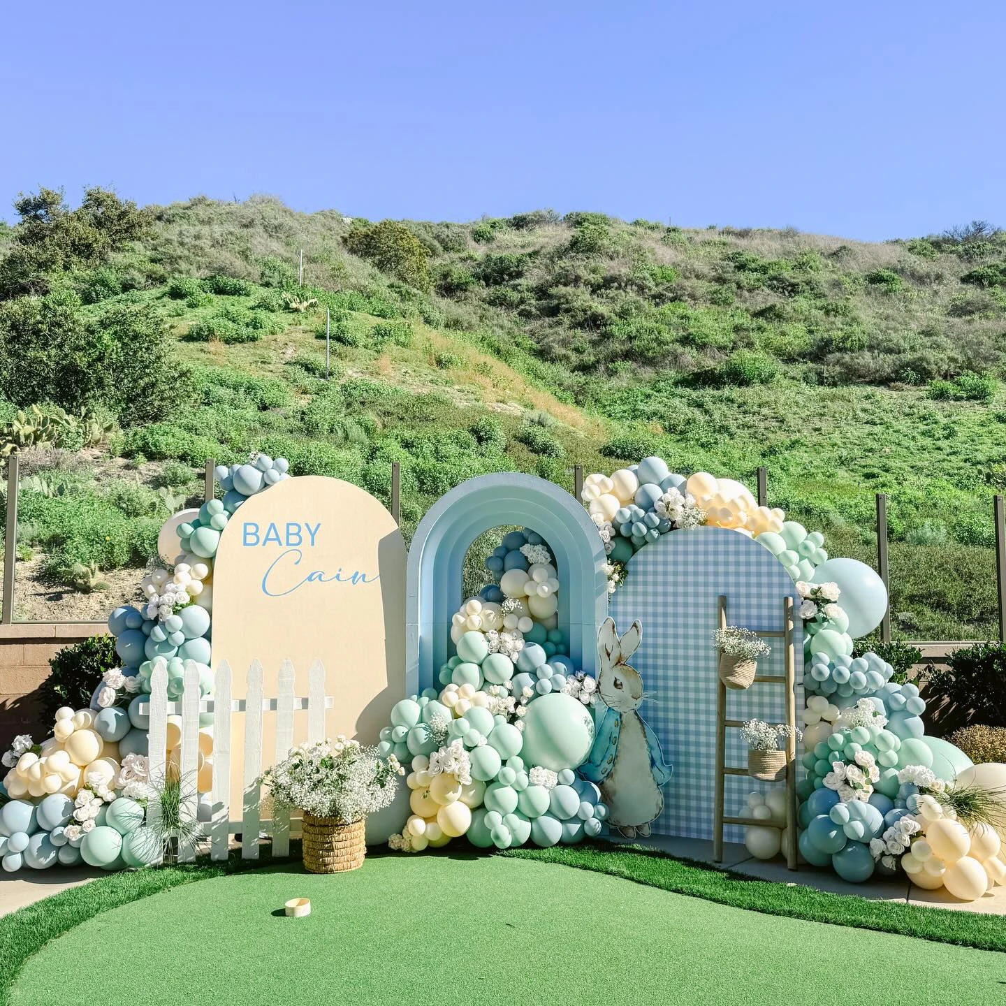 Peter Rabbit baby shower backdrop with pastel balloons and a white picket fence.