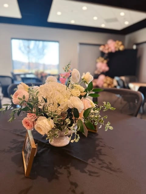 A floral centerpiece with pink and white flowers on a table with a black tablecloth for a retirement party.