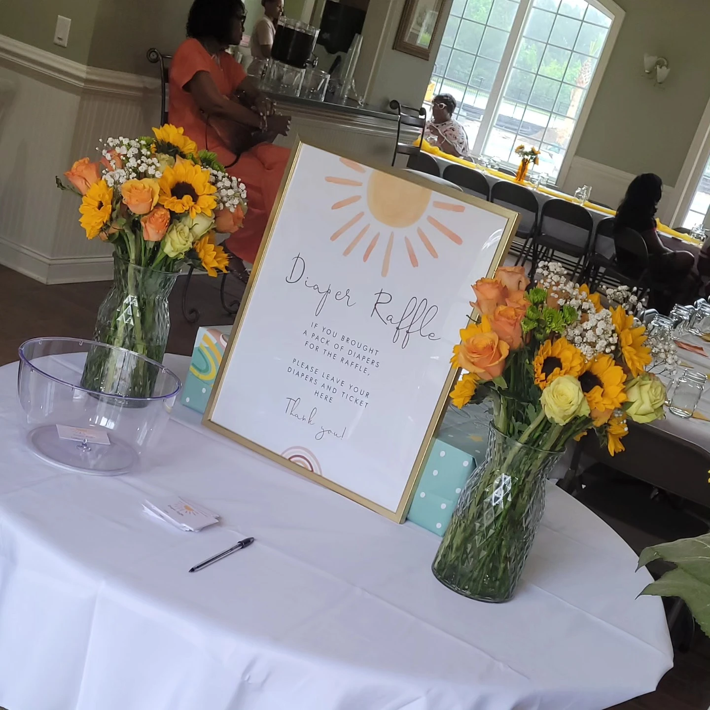 Diaper raffle sign with a sun graphic on a table with sunflower bouquets.