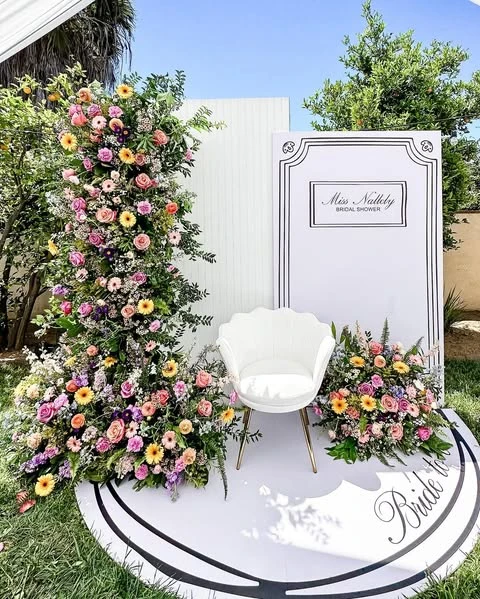 Modern bridal shower photo backdrop with a large floral arrangement and a white chair.