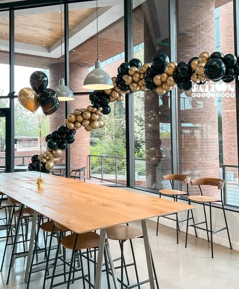 A long black and gold balloon garland hung above a communal table in a party space.