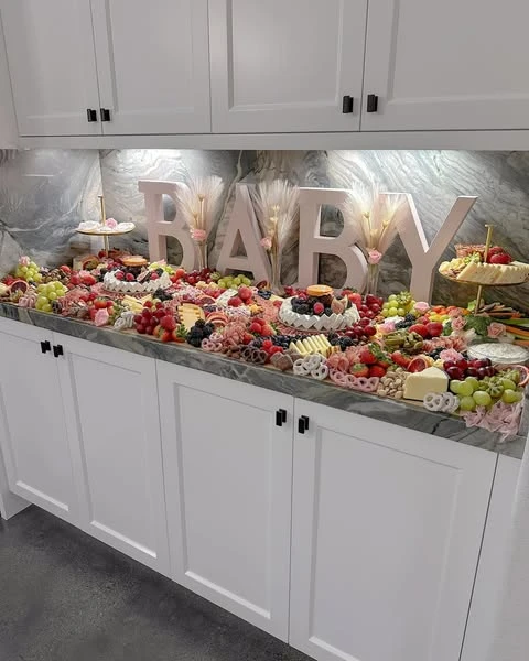 A wide view of a baby shower food table setup, showing a long grazing spread on a kitchen counter.