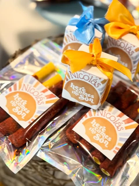 Assorted 'Here comes the Son' baby shower favors, including small boxes and cellophane bags, unified with matching sun-themed stickers.