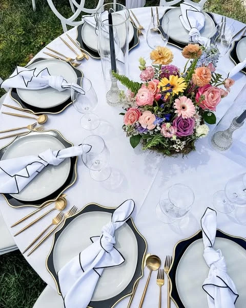 Overhead view of a modern spring bridal shower tablescape with black chargers and a colorful centerpiece.