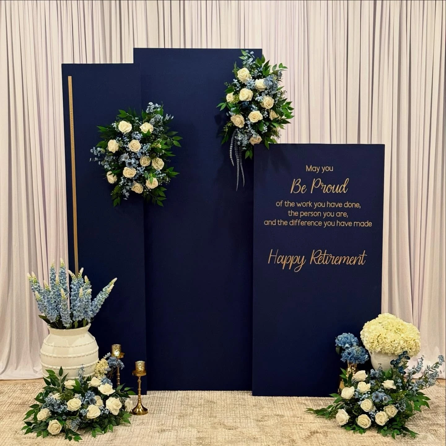 Elegant navy blue retirement party backdrop with a heartfelt quote in gold lettering and floral arrangements.