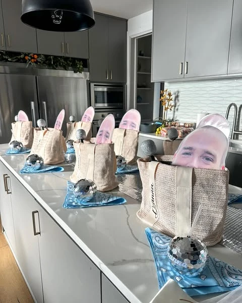 Personalized jute favor bags for a Mamma Mia bachelorette party lined up on a kitchen counter, each with a blue bandana and a mini disco ball.