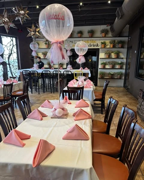 A tall baby shower centerpiece on a guest table, featuring a large clear balloon with the name 'Natalia' on it, wrapped in pink tulle.