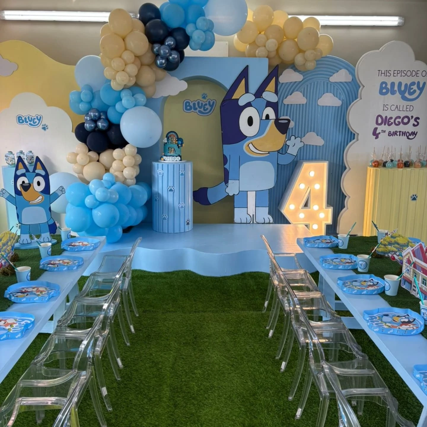 Full Bluey birthday party setup with a decorated stage, character cutouts, and long tables for guests.
