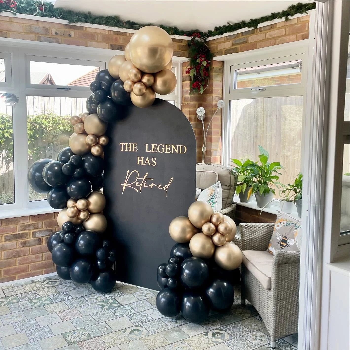 A black arched backdrop with gold text reading 'The Legend Has Retired', framed by an elegant black and gold balloon garland.