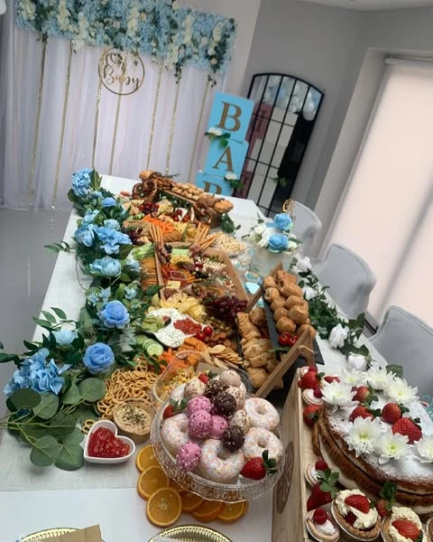 A long baby shower food table setup featuring a grazing runner with charcuterie, cheeses, donuts, and cakes.