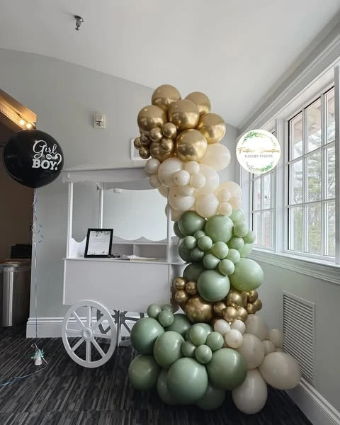 A white vintage-style dessert cart decorated with a large balloon garland in sage green, matte white, and chrome gold.