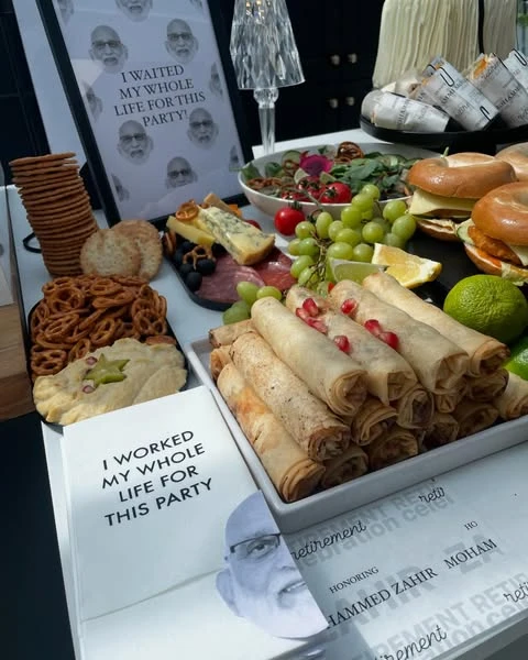 A retirement party food table with a custom sign featuring the retiree's face and a funny quote.