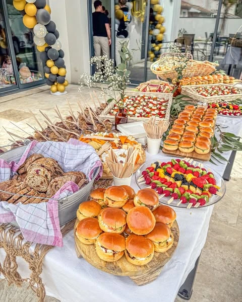 An abundant baby shower food table featuring platters of mini sliders, fruit skewers, and baskets of sliced bread.