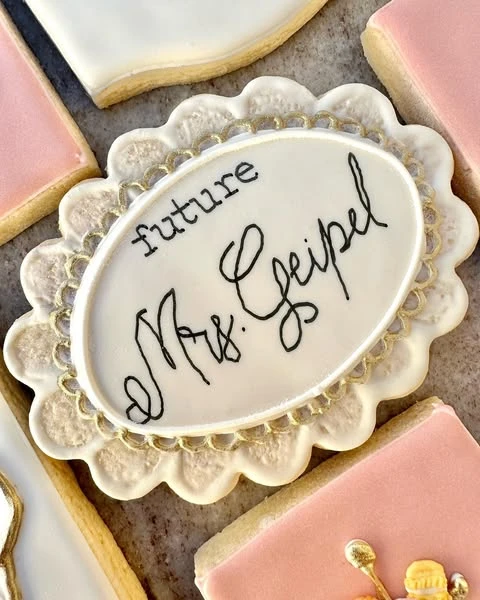 A personalized cookie for a bride-to-be with a scalloped gold edge.