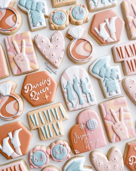 Assortment of Mamma Mia themed bachelorette party cookies in pink, terracotta, and blue.