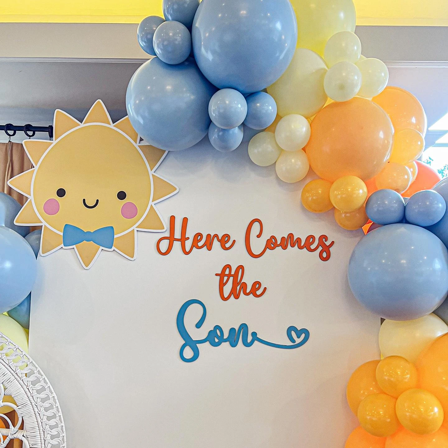 of a 'Here Comes the Son' sign and a smiling sun cartoon on a baby shower backdrop.
