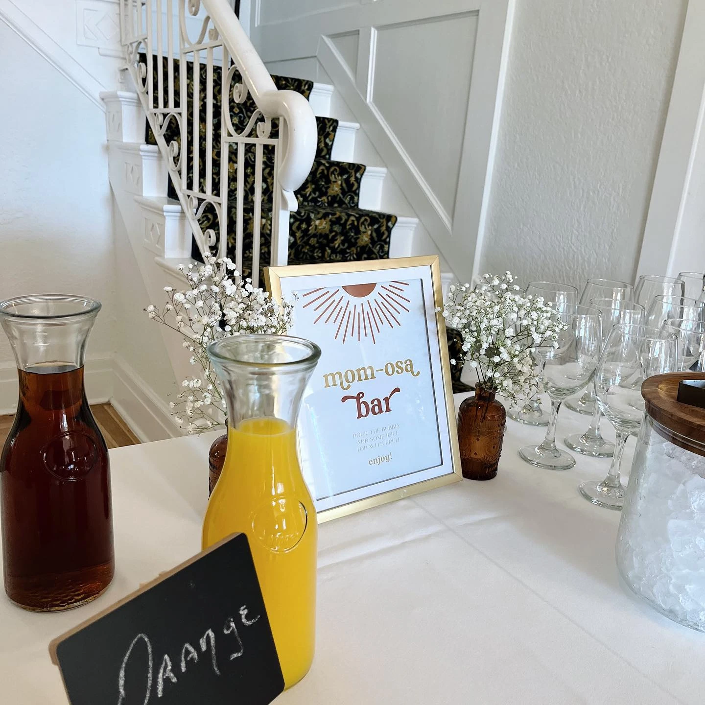 A 'mom-osa' bar for a sun-themed baby shower with juice carafes and a framed sign.