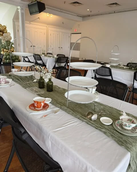 Guest table at a baby shower with a white tablecloth and a sage green gauze runner.