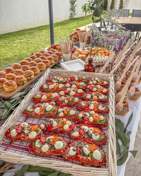 A baby shower food table with wicker appetizer trays holding tomato and mozzarella bites next to mini sliders.