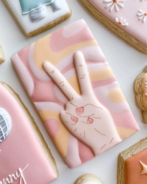 A 70s-style peace sign cookie with a pink and peach swirl background.