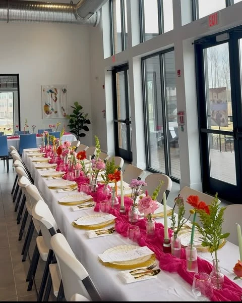 A long reception table decorated for a spring bridal shower with a pink runner and individual flower vases.