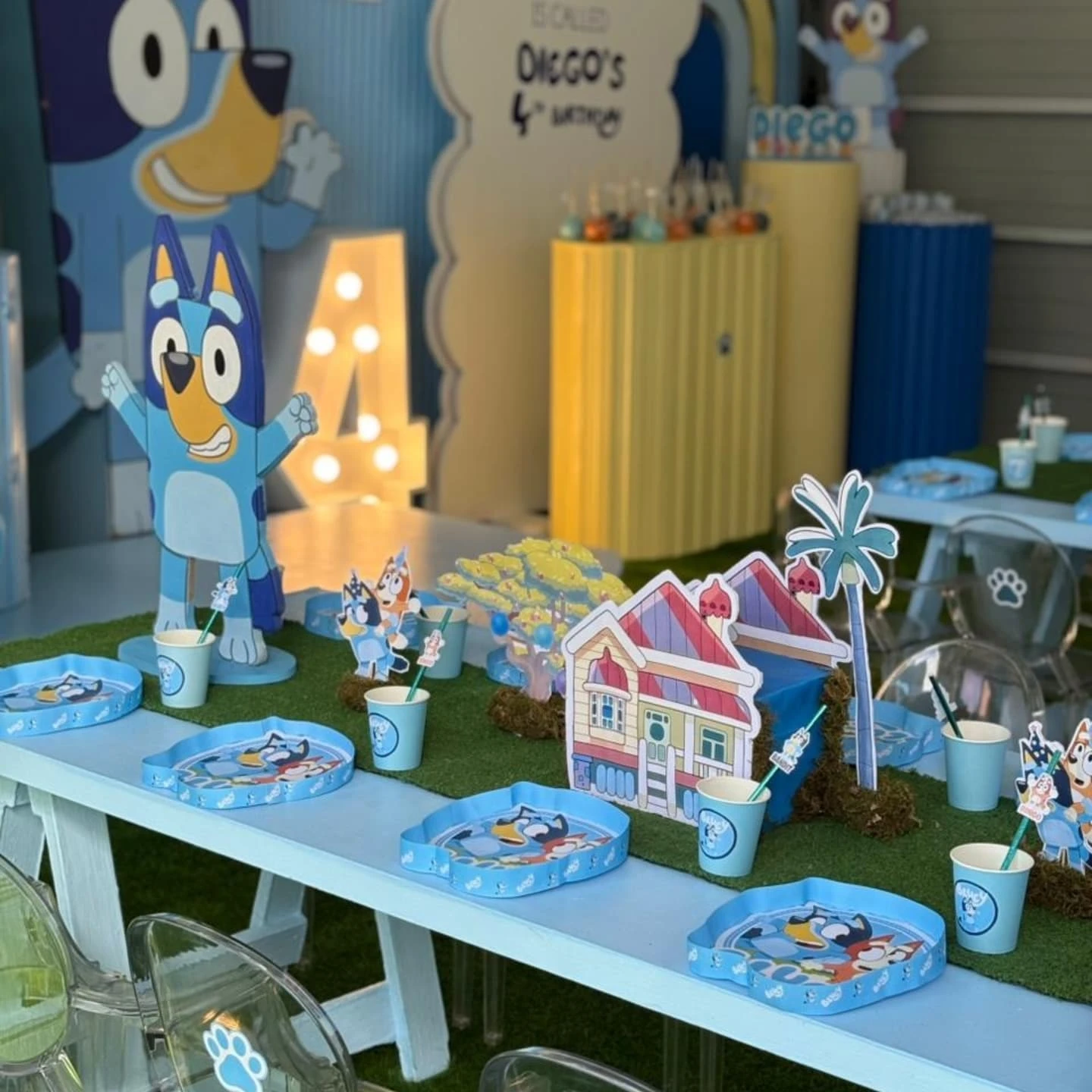A of a kids' party table setting with Bluey paper plates and a centerpiece shaped like Bluey's house.