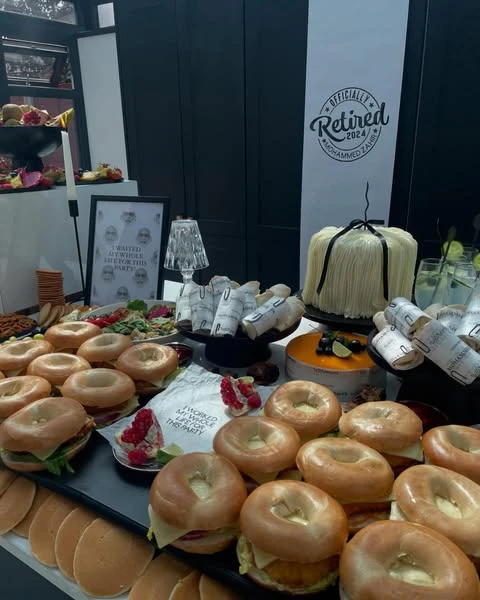 A wide view of a brunch-style buffet for a retirement party, featuring bagels and cakes.