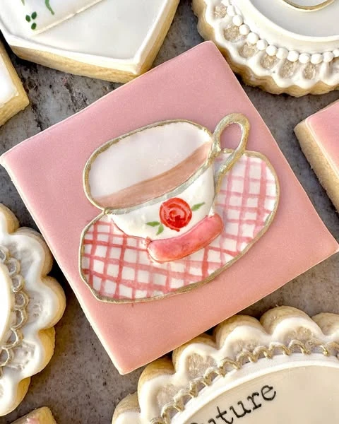 A square pink cookie with a teacup and gingham saucer design.