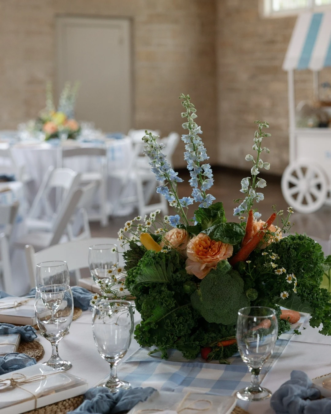 A table centerpiece for a Peter Rabbit baby shower made with fresh kale, carrots, and light blue flowers.